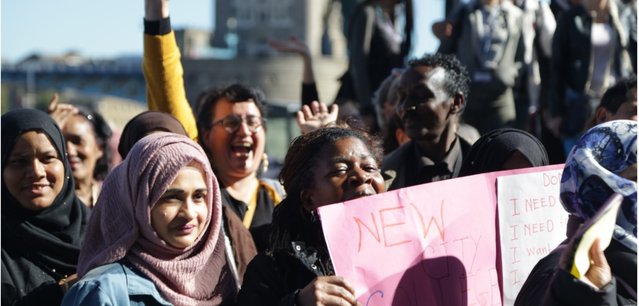 Community Organisers-Diverse group of people on a march near Tower Bridge. One person is holding a big sign.