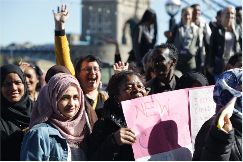 Community Organisers-Diverse group of people on a march near Tower Bridge. One person is holding a big sign.